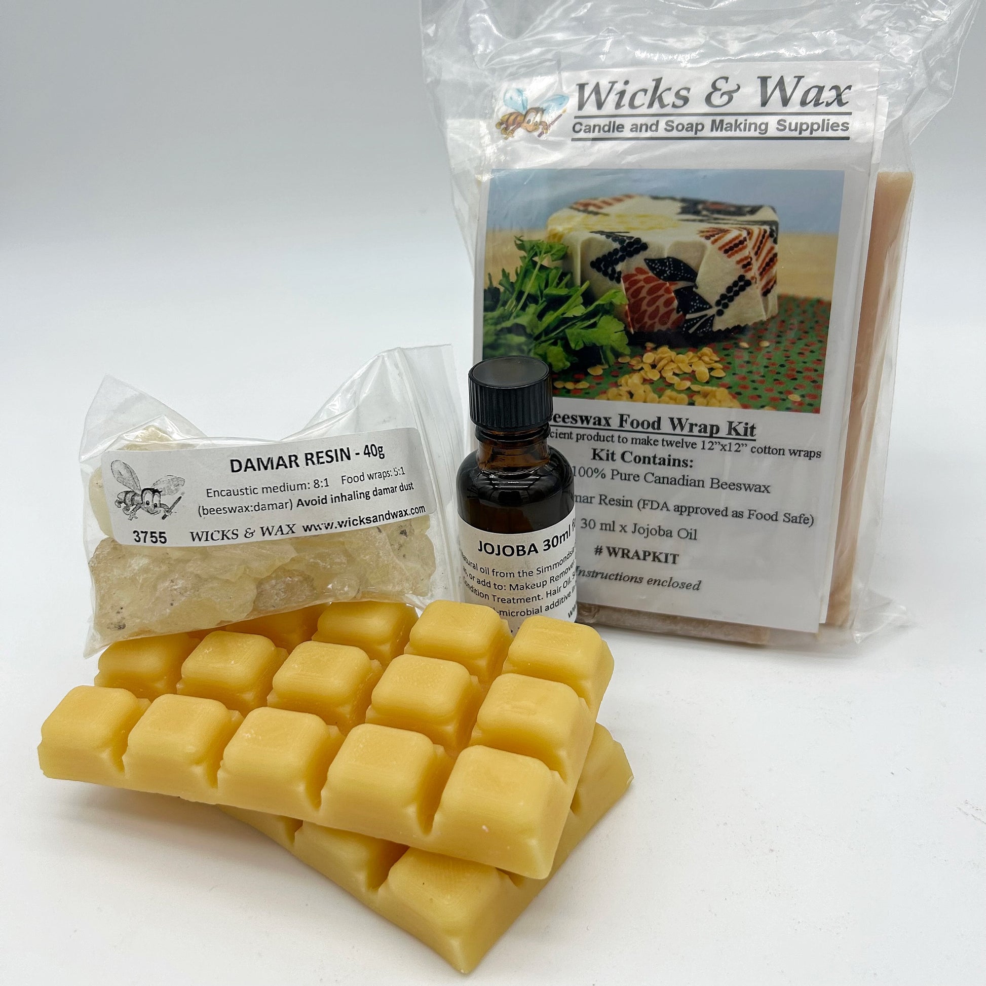 Wax melts, resin, and a bottle of Jojoba Oil with Wicks & Wax packaging on a white background